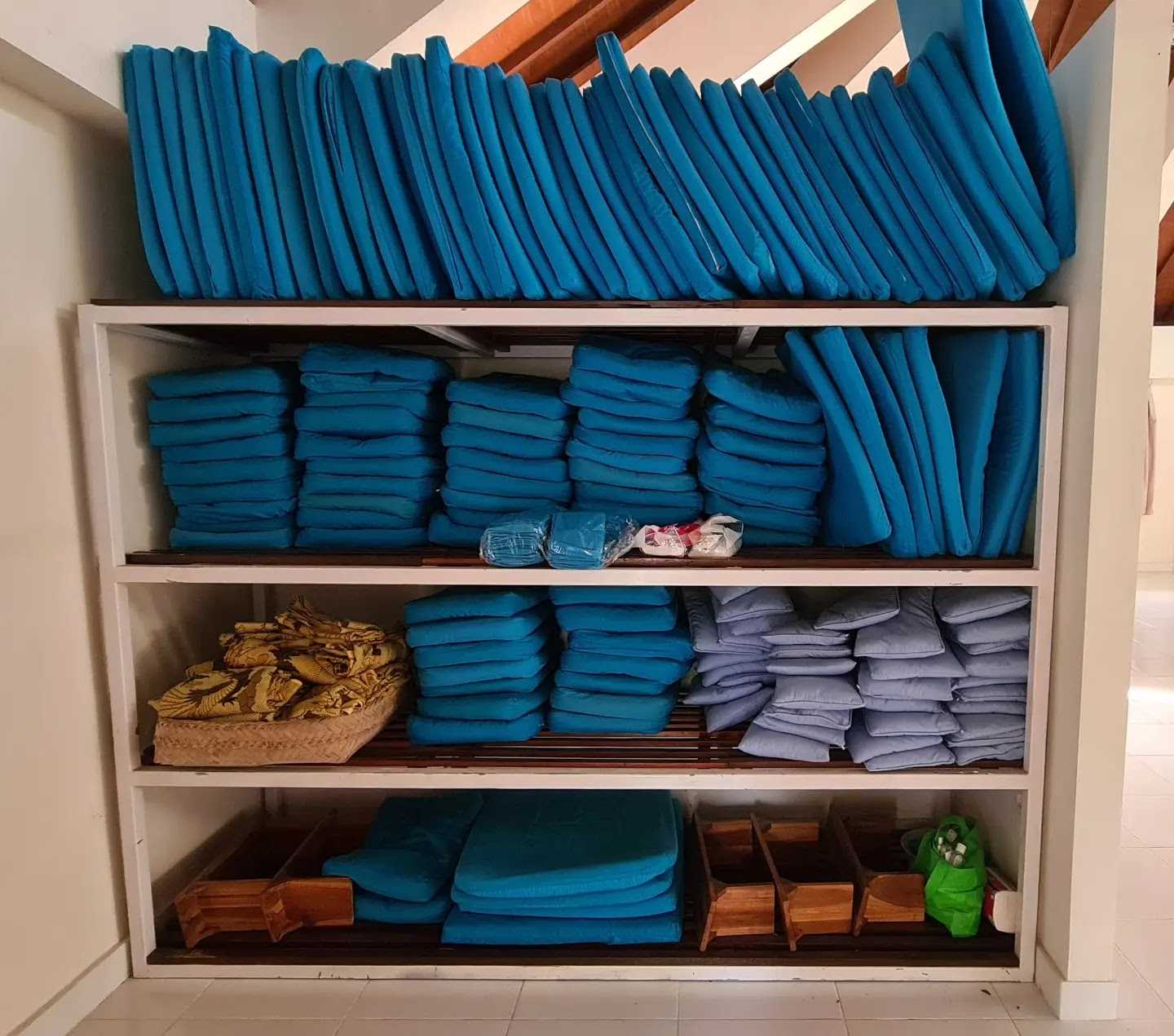 A shelf stacked with blue meditation cushions and mats of various sizes, plus smaller light-blue pillows and a few wooden meditation benches