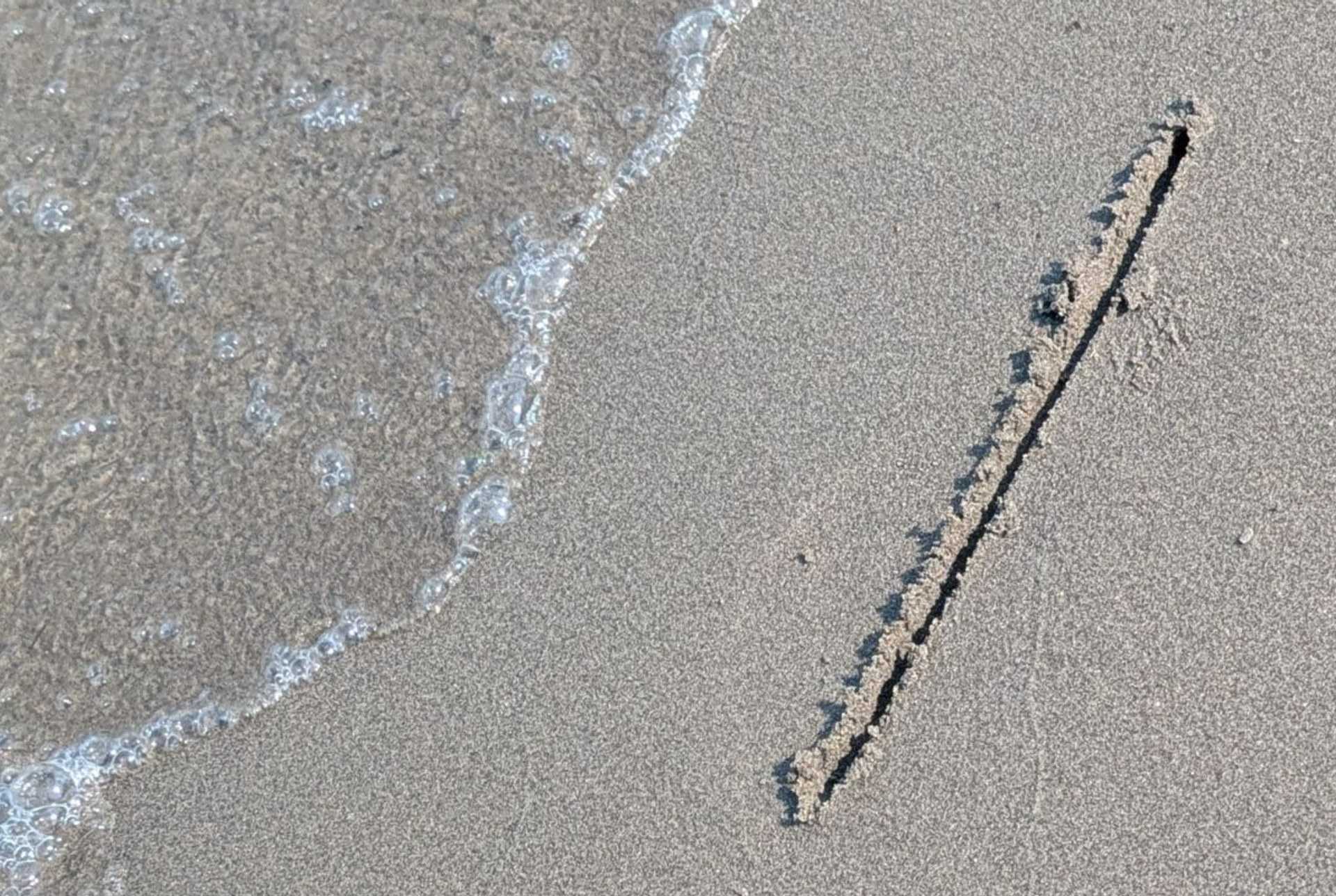 A single short line drawn in wet beach sand, with the edge of a wave washing up beside it
